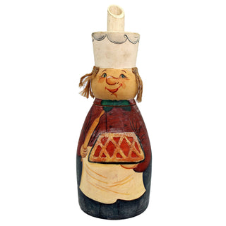 A wooden figurine depicting a smiling chef or baker, wearing a chef's hat and holding a tray of baked goods.