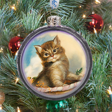 A glass ornament with a painting of a cat sitting on a plate, surrounded by Christmas decorations.
