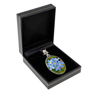 A black jewelry box containing a pendant with a floral design, including blue and purple flowers.
