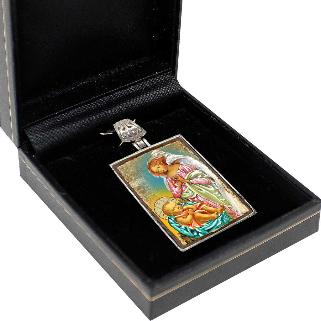 A pendant with a religious scene, possibly depicting the birth of Jesus Christ, is displayed in a black jewelry box.