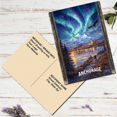 a postcard with a painting of a scenic landscape, including mountains, a lake, and a colorful sky with the Aurora Borealis. The postcard is placed on a white wooden surface, and there are some purple flowers nearby.