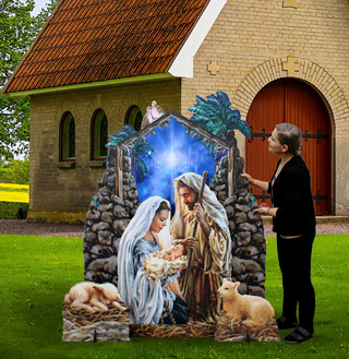 A woman is standing next to a large cardboard cutout depicting the Nativity scene, with a man, baby Jesus, and other figures in a manger.