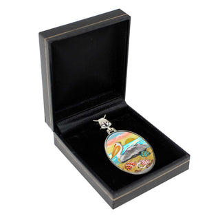 A pendant in a black jewelry box, featuring a colorful design depicting a bird and a landscape.