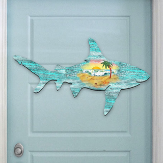 A wooden shark sculpture is mounted on a light blue door, depicting a tropical beach scene with palm trees, a sandy beach, and a sunset.