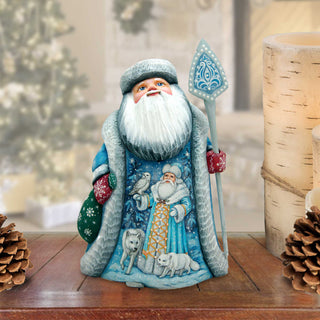 A figurine of Santa Claus holding a snowshoe and a reindeer, with a wreath and pine cones in the background.