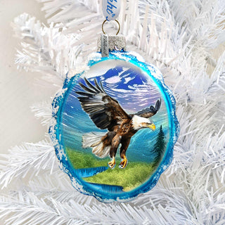 A blue ornament with a picture of a bald eagle in mid-flight, surrounded by a snowy landscape.