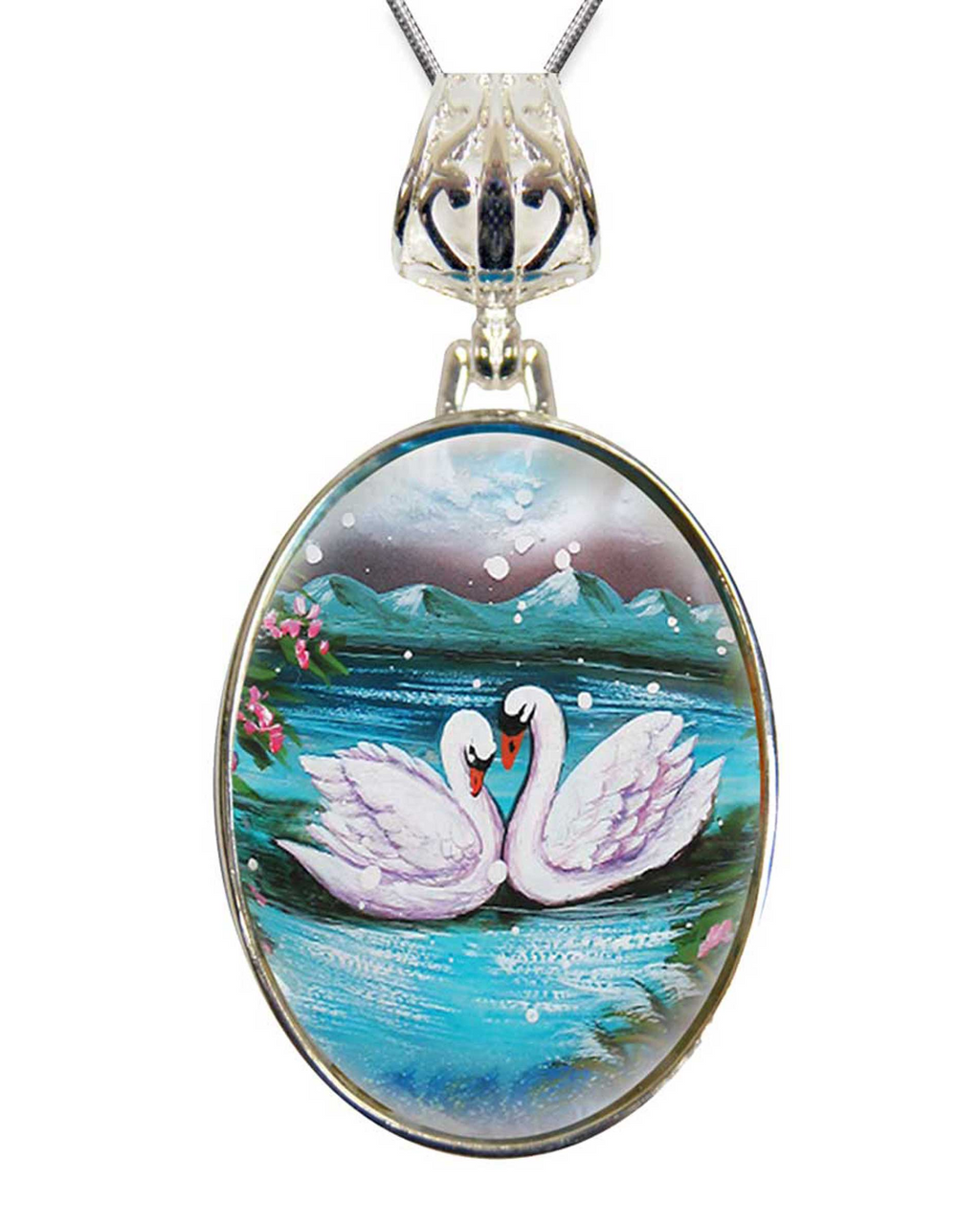 A pendant necklace with a circular oval-shaped design featuring two swans swimming in a body of water, surrounded by flowers and mountains in the background.