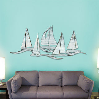 a wall art display of several white sailboats on a blue wall, with a gray couch in the foreground.