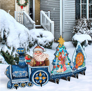 A festive Christmas scene with a decorated train carrying a Santa Claus figure, surrounded by snow-covered bushes and a house.