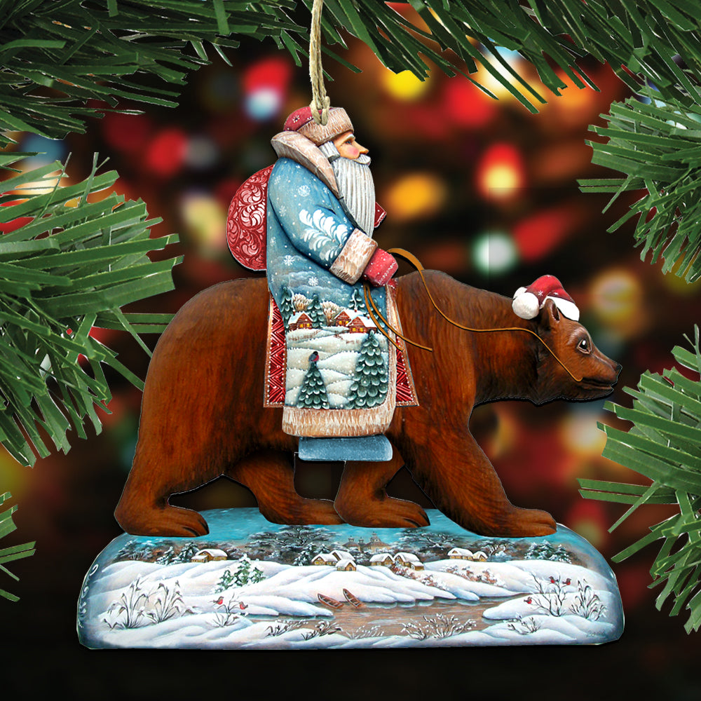 A Christmas ornament depicting Santa Claus riding a bear, with a snowy landscape and trees in the background.