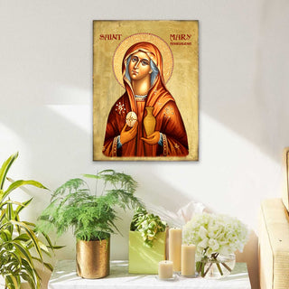 a religious icon of St. Mary of the Flower, displayed on a wall above a table with potted plants and candles.