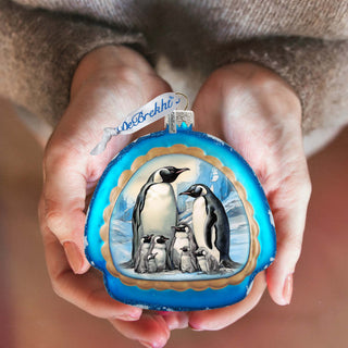 a person holding a christmas ornament with penguins on it