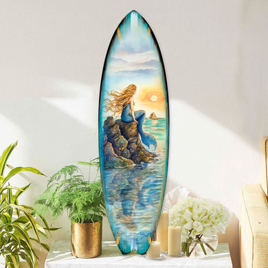 Handcrafted Mermaid Surfboard Wall Art by G. DeBrekht, featuring a mystical mermaid gazing at a sunset from a rocky perch. Perfect coastal wall decor for beach house interiors, surf-inspired spaces, and nautical-themed rooms. UV-coated for indoor & outdoor display