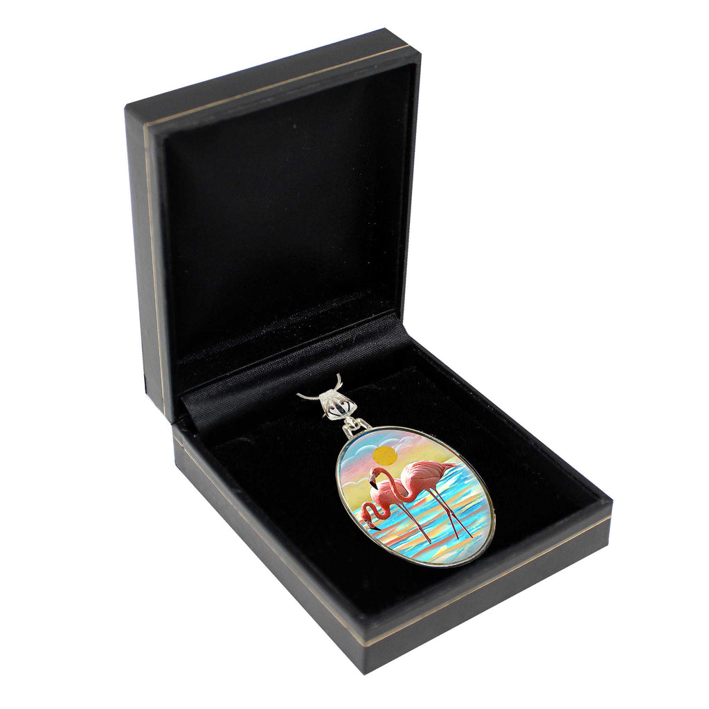 A pendant with a colorful design, featuring a flamingo and a sunset, is displayed in a black jewelry box.