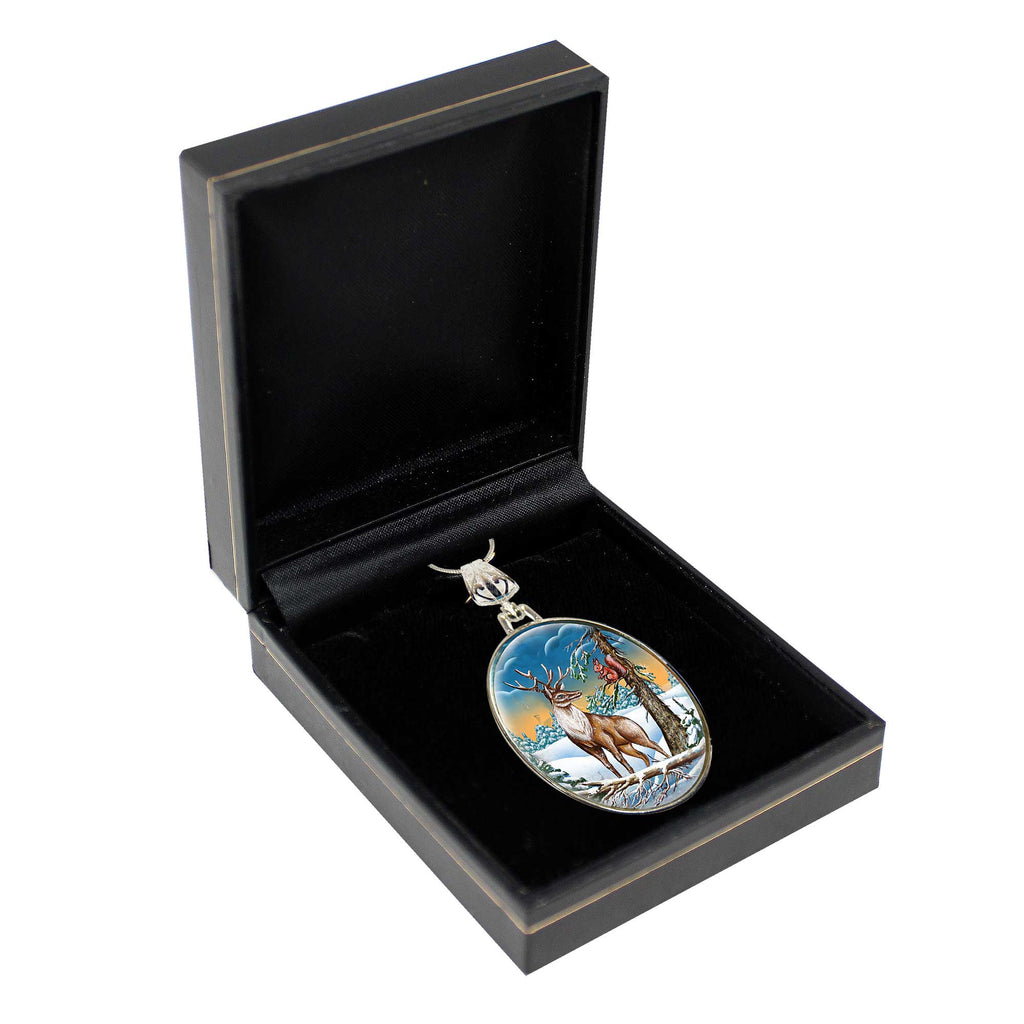 A pendant in a black jewelry box, featuring a deer and a snowy landscape.