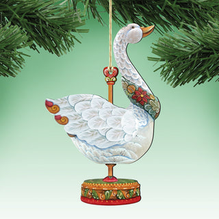 A decorative ornament of a white swan with a red and gold base, hanging from a string and placed on a branch of a Christmas tree.
