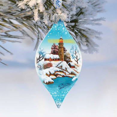 A blue glass ornament hanging from a tree branch, depicting a snowy winter landscape with a lighthouse in the distance.