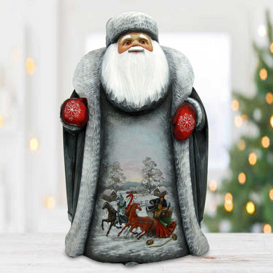 A figurine of Santa Claus sitting on a wooden surface, with a snowy landscape and a sleigh pulled by reindeer visible on the figurine.