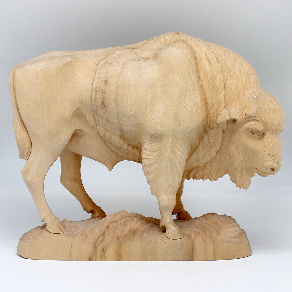 A wooden carving of a buffalo, likely a bison, standing on a rock.