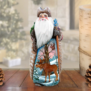 A wooden Santa Claus figurine holding a reindeer and a snowman, set against a snowy winter landscape.