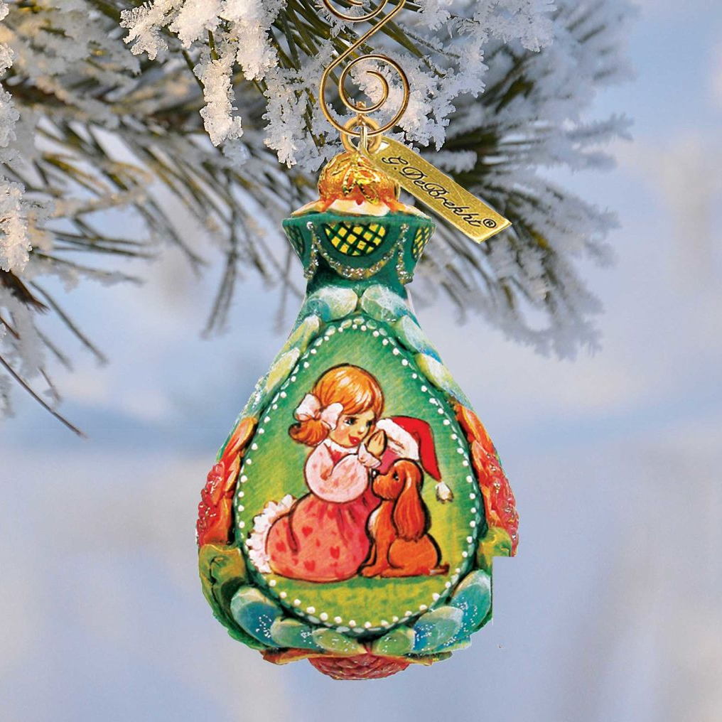 A colorful ornament featuring a girl and a dog, hanging on a snowy branch of a tree.
