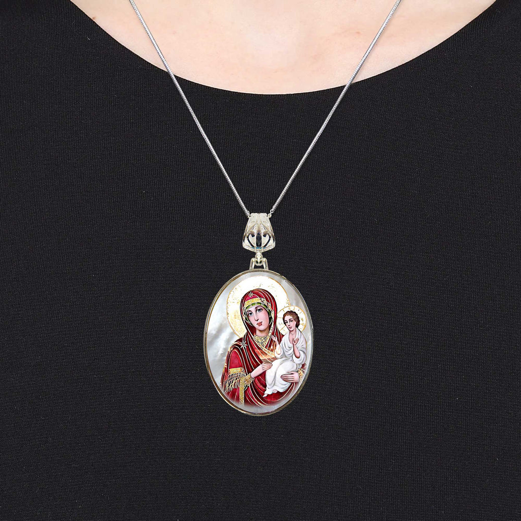 A silver necklace with a pendant featuring an image of a woman in a red robe and holding a baby.