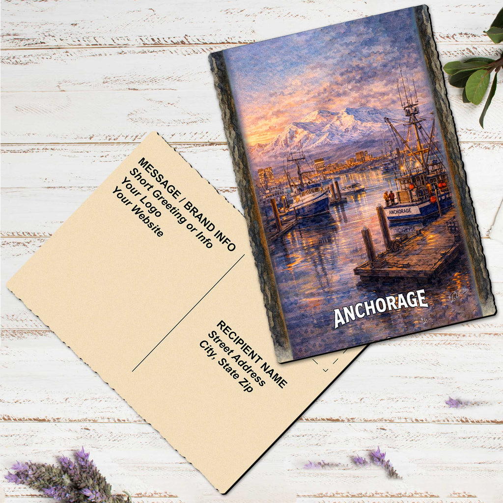 a postcard with a painting of a harbor scene, including boats and a mountain in the background. The postcard is placed on a white wooden surface, with some purple flowers nearby.