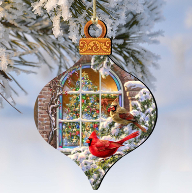 A decorative ornament featuring a snowy scene with two red cardinals perched on a branch, with a Christmas tree and a window visible through the branches.
