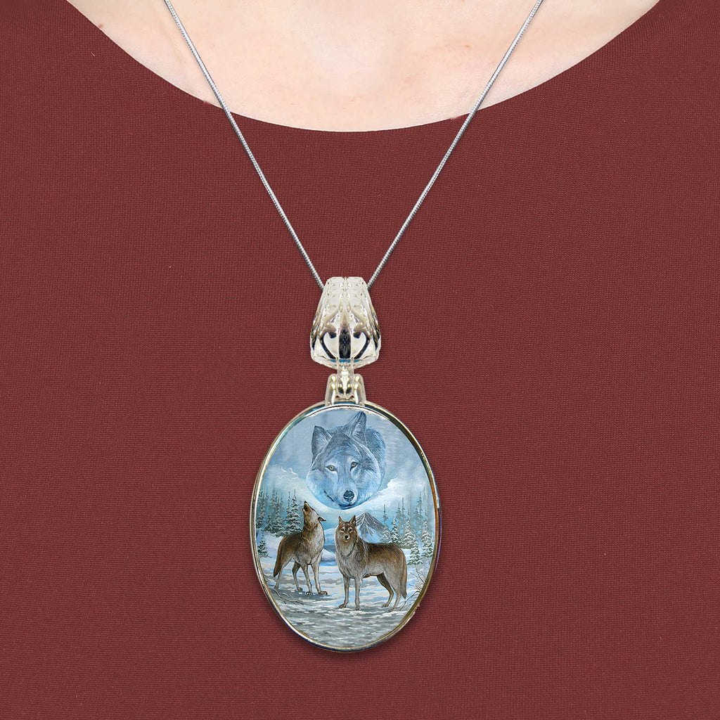 A necklace with a pendant featuring a painting of two wolves in a snowy landscape.