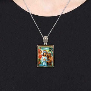 A silver pendant necklace with a rectangular pendant featuring religious imagery.