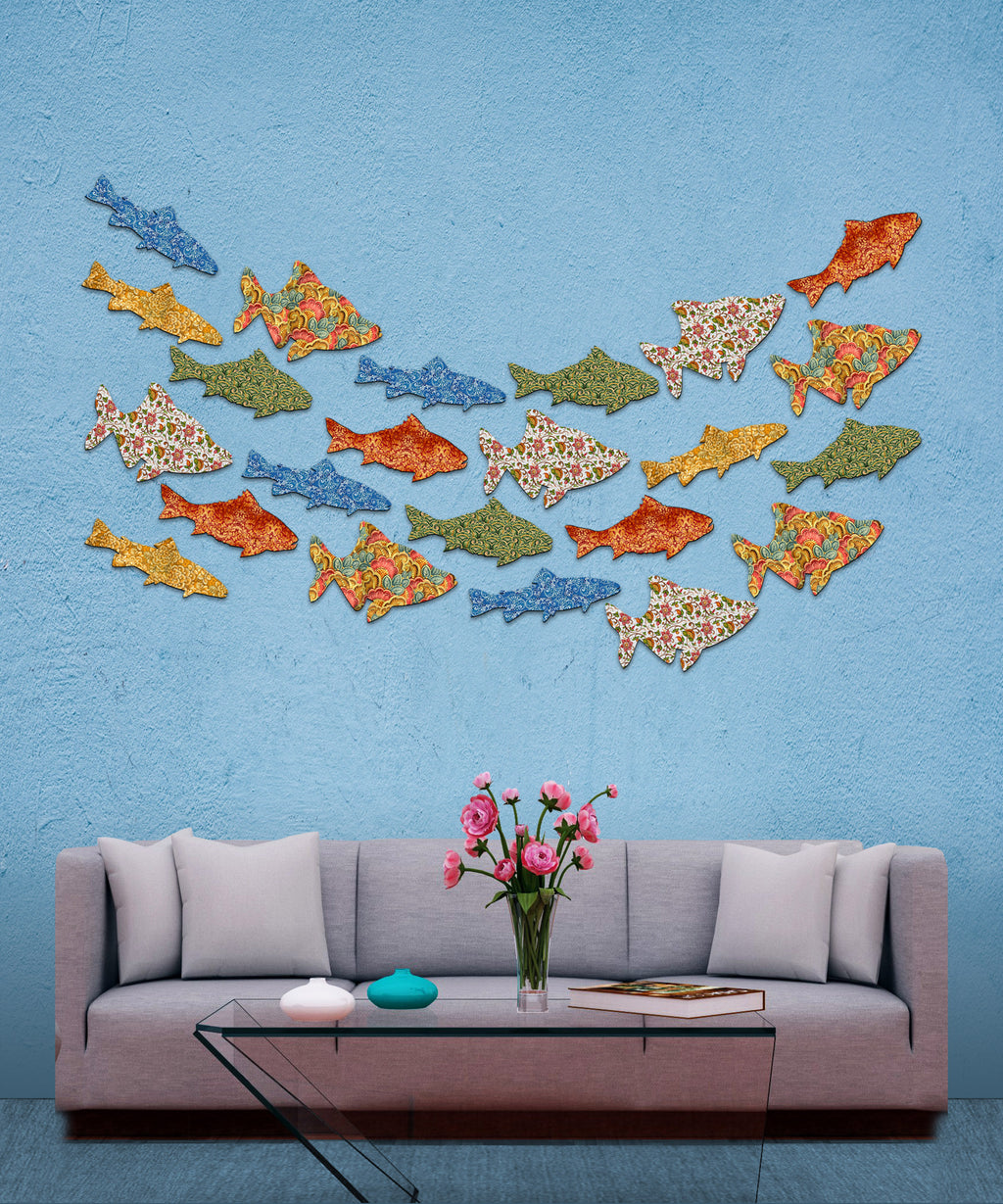 a cozy living room with a gray sofa, a glass coffee table, and a vase of pink flowers. Above the sofa, there is a wall adorned with a collection of colorful fish-shaped wall art, creating a vibrant and playful atmosphere.