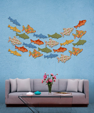 a cozy living room with a gray sofa, a glass coffee table, and a vase of pink flowers. Above the sofa, there is a wall adorned with a collection of colorful fish-shaped wall art, creating a vibrant and playful atmosphere.