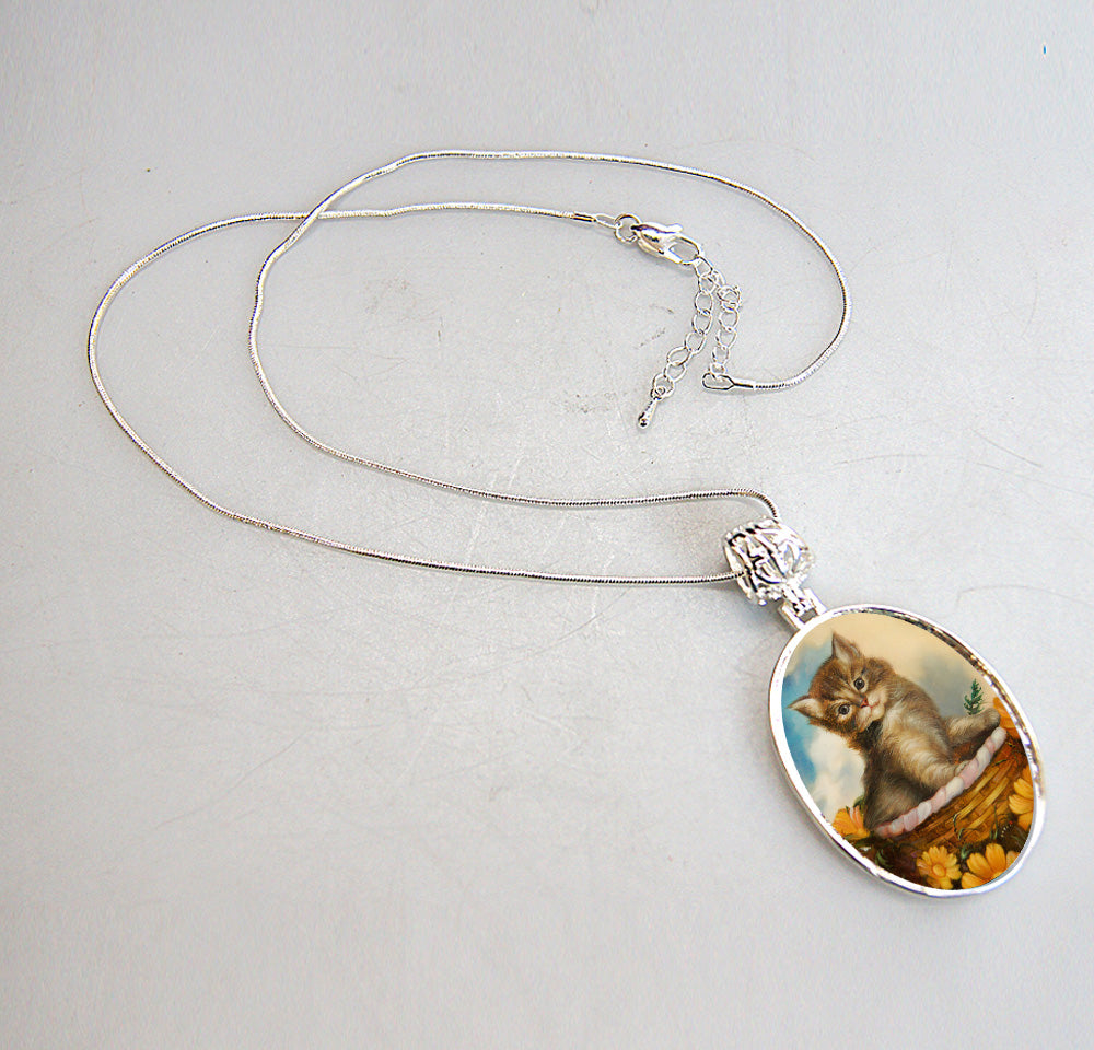 A silver necklace with a pendant featuring a small kitten sitting in a basket.