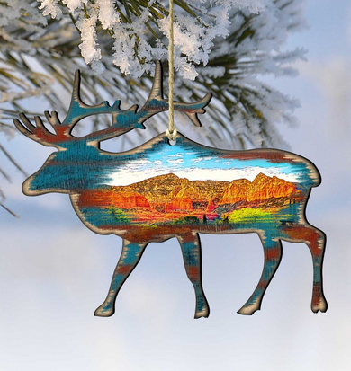 A wooden ornament in the shape of a deer, with a colorful landscape painted inside, hangs from a string against a snowy background.