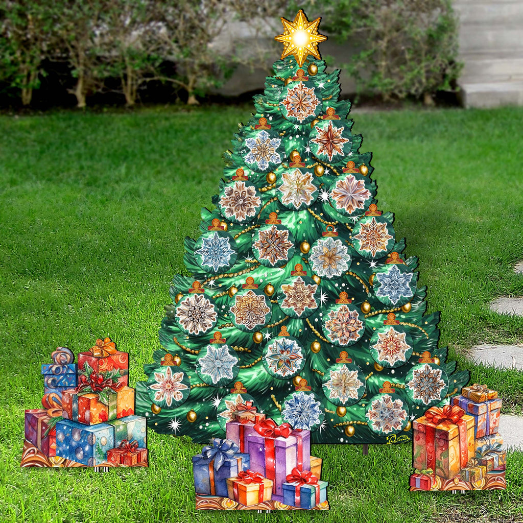 A large, colorful Christmas tree made of various materials, including cardboard and paper, stands in a grassy area surrounded by wrapped gifts.