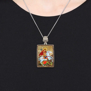 A silver necklace with a rectangular pendant featuring a religious scene.