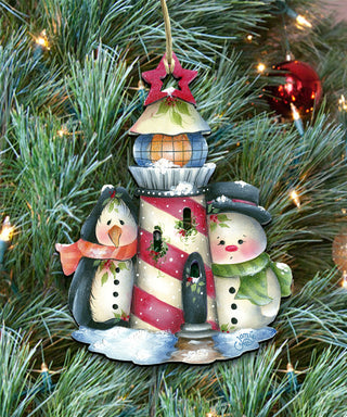 A colorful ornament featuring a lighthouse, two snowmen, and a star, hanging on a Christmas tree.