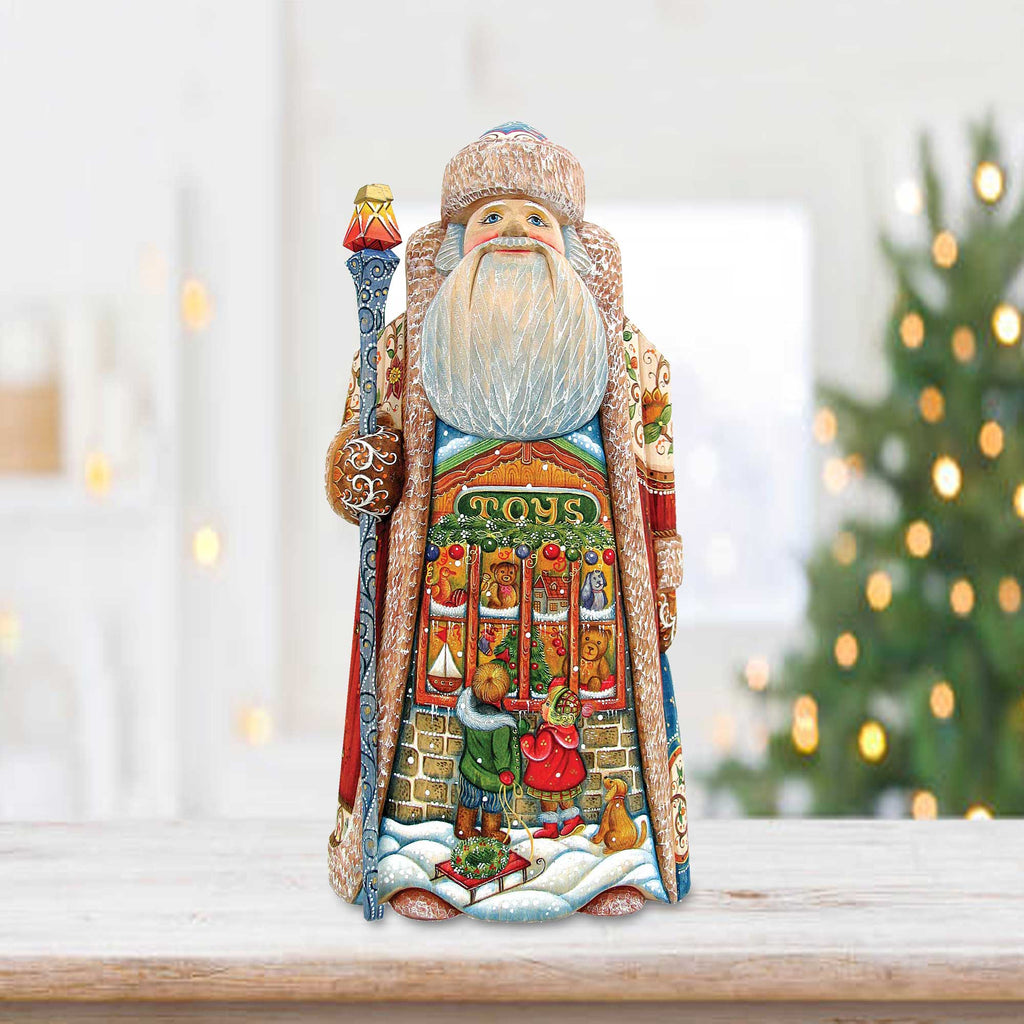 A detailed figurine of Santa Claus holding a staff and a bag of toys, standing on a wooden surface with a blurred background featuring a Christmas tree.