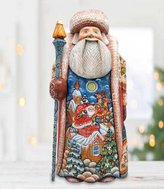 A colorful and intricately carved wooden Santa Claus figurine, featuring detailed designs of a snowy village, a moon, and a starry night sky.