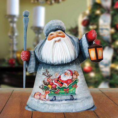 A wooden Santa Claus figurine holding a lantern and a reindeer, with a snowy background and a blurred Christmas tree in the background.