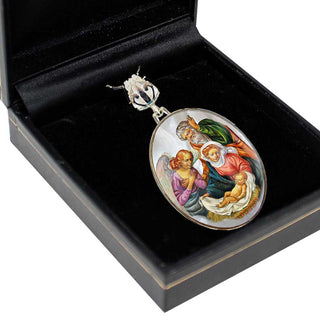 A pendant with a religious scene, featuring a baby Jesus surrounded by people, is displayed in a black jewelry box.