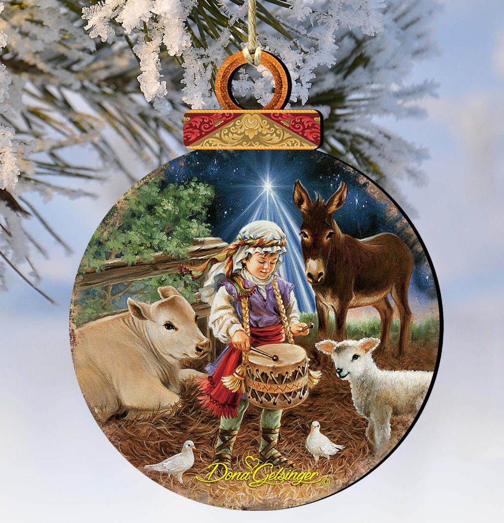 A Christmas ornament depicting a young boy playing a drum, surrounded by animals such as a donkey, sheep, and a cow, with a starry night sky in the background.