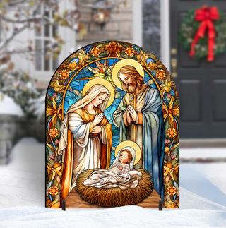 A stained glass nativity scene depicting the baby Jesus, Mary, and Joseph in a manger, surrounded by flowers and a wreath.