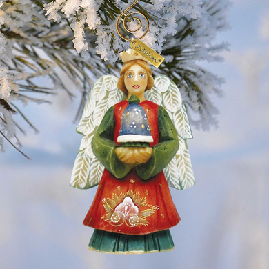 A Christmas ornament in the shape of an angel, with a crown on its head, is hanging on a tree branch covered in snow.