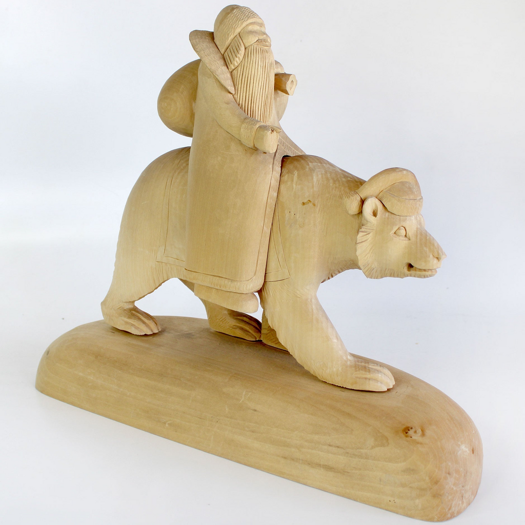 A wooden carving depicting a man riding a bear on a wooden platform.