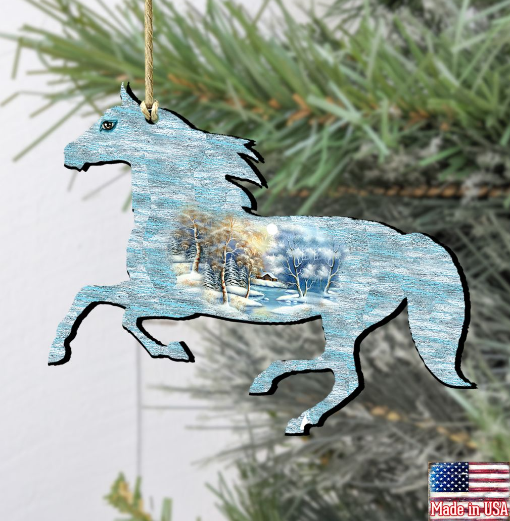 A wooden ornament in the shape of a horse, with a winter landscape scene inside, hanging on a tree branch.