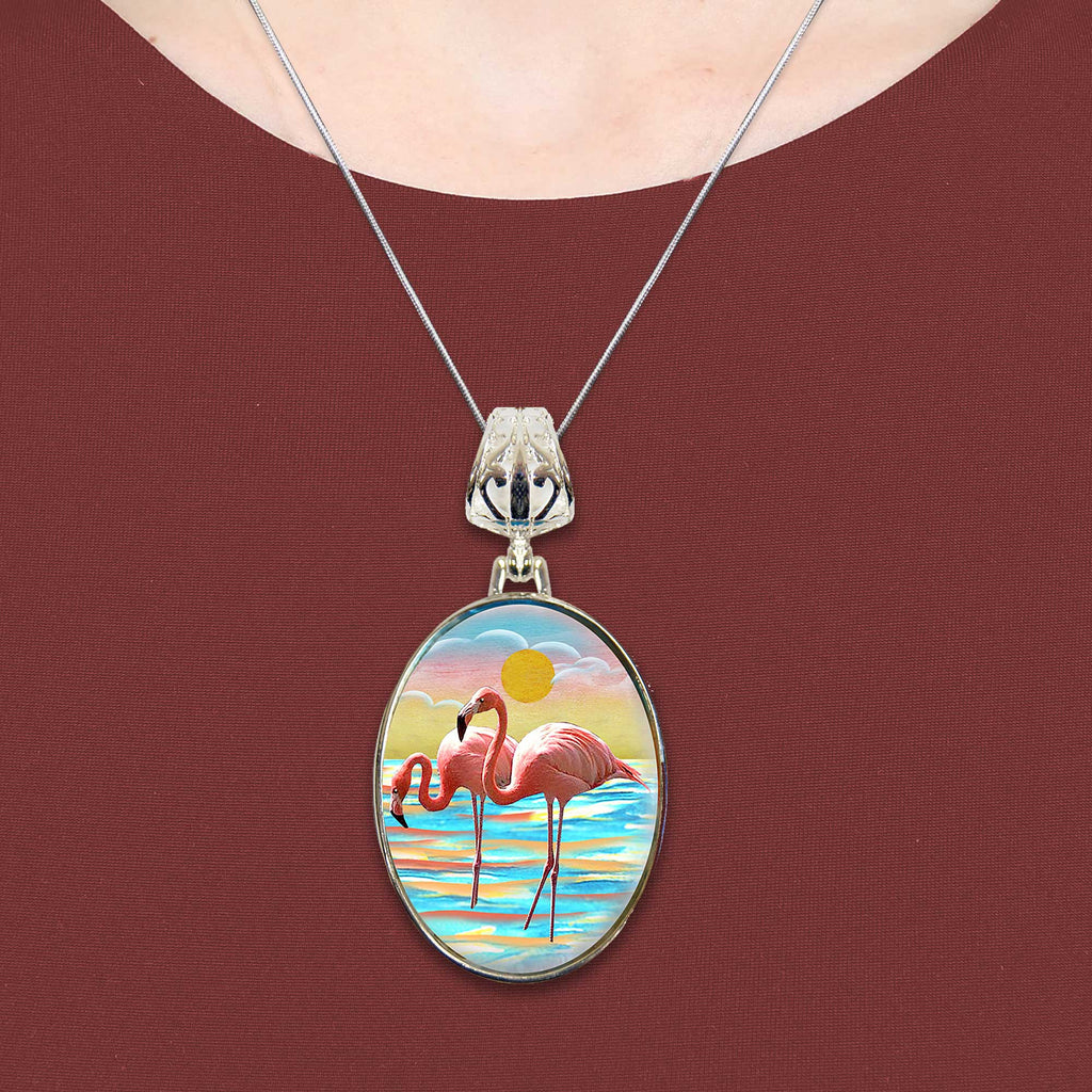 A necklace with a pendant featuring a painting of two flamingos in a serene beach scene.