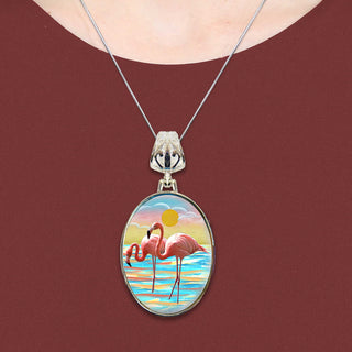 A necklace with a pendant featuring a painting of two flamingos in a serene beach scene.