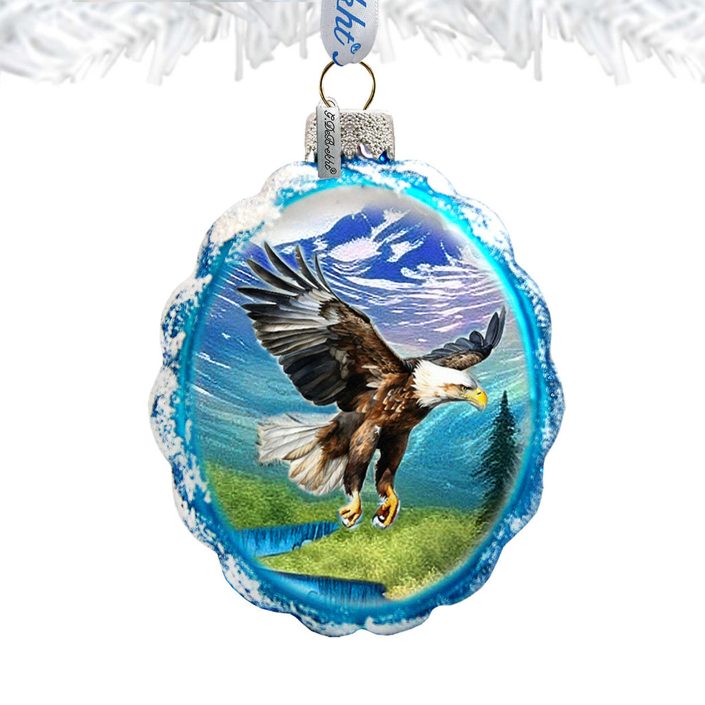 A glass ornament with a blue and white design depicting an eagle in flight against a mountainous landscape.