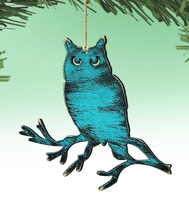 A blue owl ornament is hanging from a string against a green background.